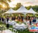 Outdoor wedding reception setup under a white high peak commercial tent in New Jersey featuring guest round tables, patio heaters, a wooden dance floor, and a catering buffet