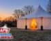 White high peak tent with closed walls glowing at dusk on a New Jersey lawn in late autumn